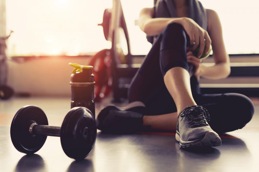 Attain at Greenbrier apartment homes with Person sitting on gym floor with a dumbbell and water bottle nearby, wearing athletic clothing and sneakers.