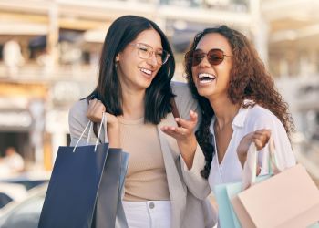 Attain on 5th apartment homes with Two women smiling and laughing while holding shopping bags outdoors on a sunny day.