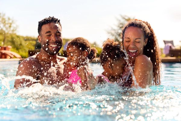 Attain on 5th apartment homes with Smiling family with two young children splashing and playing together in a swimming pool on a sunny day.