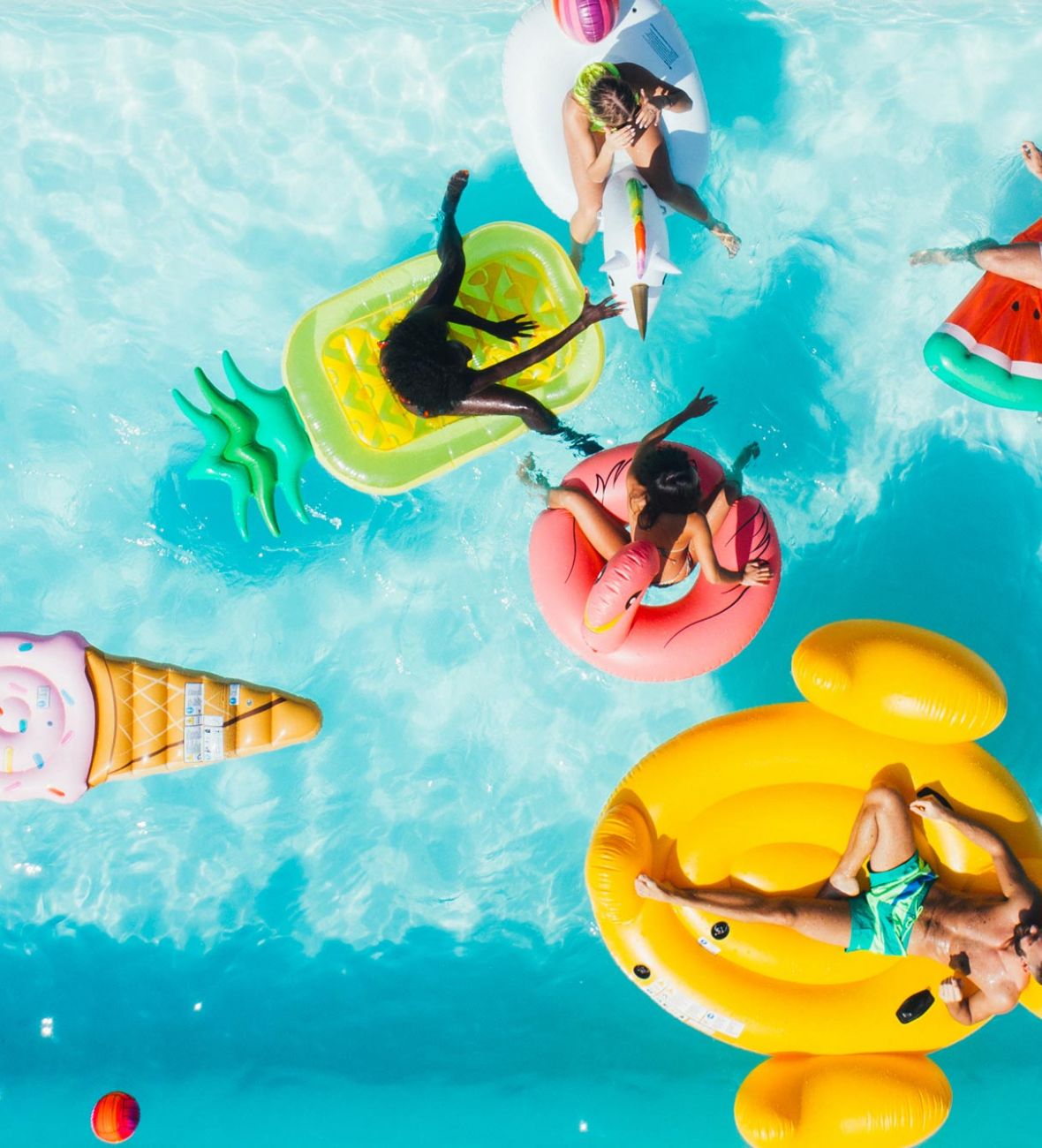 Attain on 5th apartment homes with Five people relax on colorful pool floats, including a donut, ice cream, and watermelon, in a bright blue swimming pool.