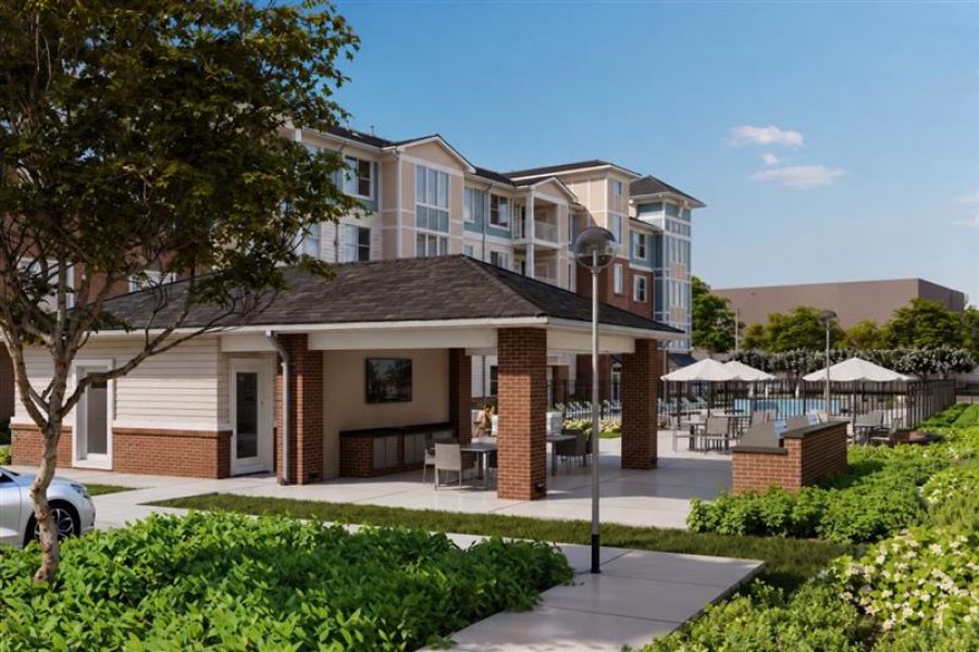 Attain on 5th apartment homes with Outdoor pavilion with tables and a grill next to a large apartment building and swimming pool area.