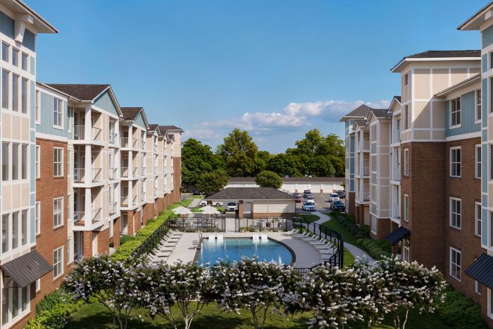 Attain on 5th apartment homes with Apartment buildings surround a courtyard with a swimming pool, lounge chairs, and trees under a clear blue sky.